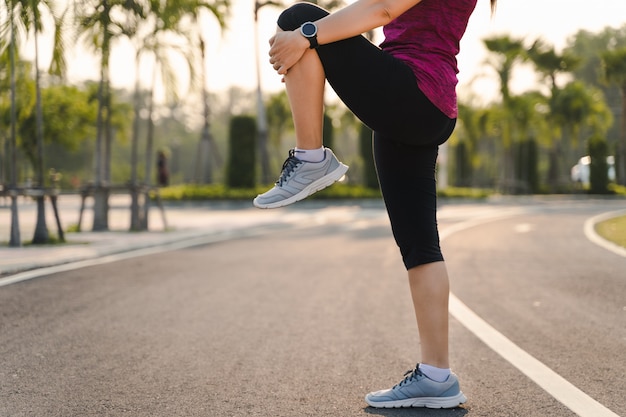 Young woman runner stretching legs before run in the park.