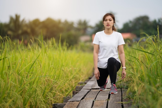 Young woman runner stretching legs before run on wooden path in field