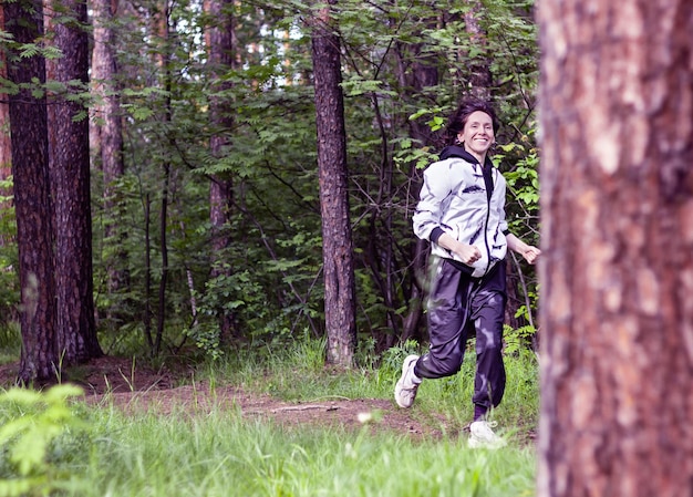 Young woman running in the forest along the path between green trees