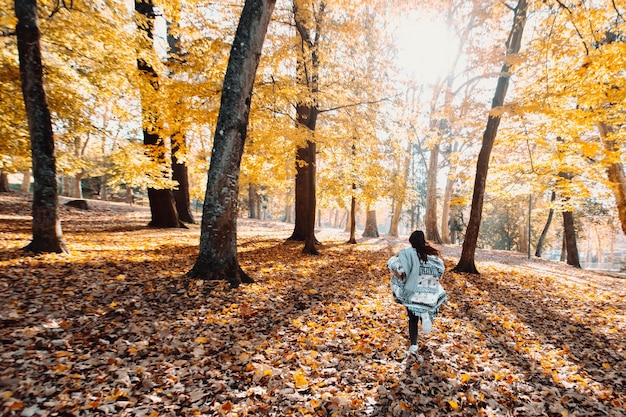 Young woman running in the forest during the autumn sunset light. Happy young woman having fun in autumn. Happy girl