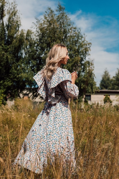 A young woman in a rustic dress stands with her back and looks into the distance