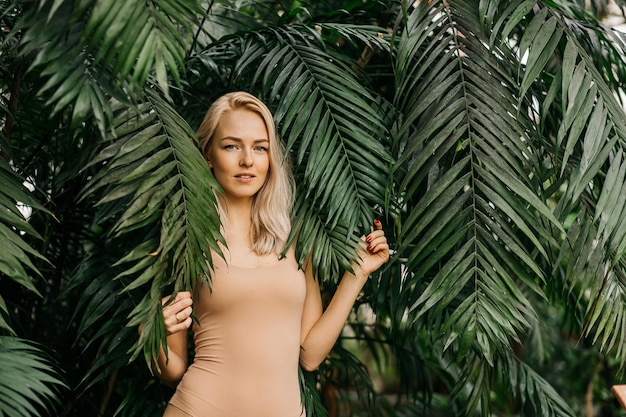 Young woman's face surrounded by tropical leaves. Closeup portrait of magnificent lady with natural nude makeup, perfect skin, blonde hair. Natural cosmetic, wellness, purity, skincare, beauty concept