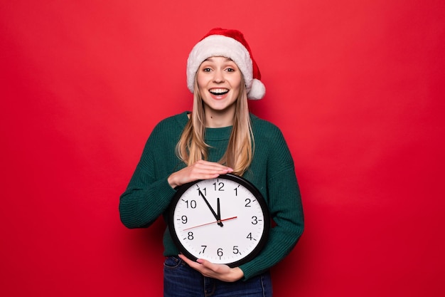 Young woman in Santa hat with clock on red wall. Christmas countdown