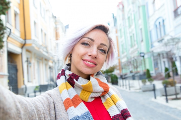 Young woman in a scarf takes a selfie against the background of the city