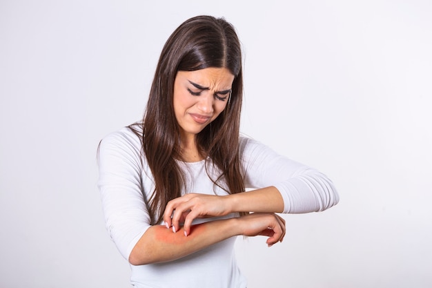 Young woman scratching her arm due to itching on a gray background.