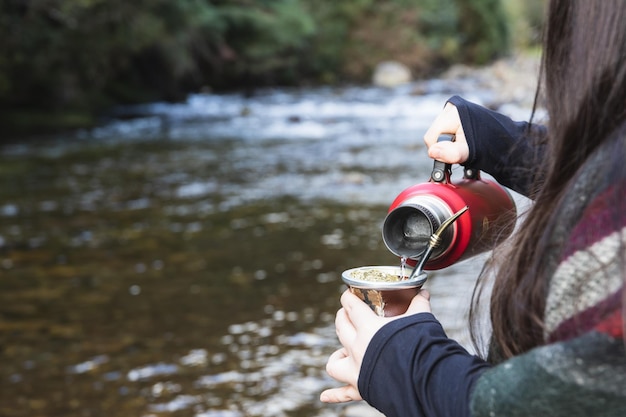 Young woman serving mate in a natural space Beside the river Latin beverage