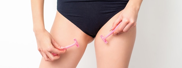 Young woman shaving crotch in bikini zone with two razors standing on white background, concept skincare and hair removal.