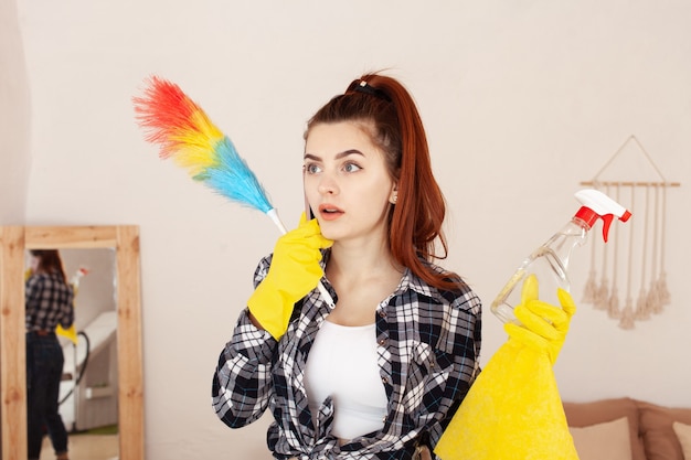 Young woman in a shirt and rubber gloves doing cleaning in the house and talking on phone