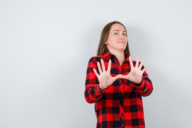 Young woman showing restriction gesture in checked shirt and looking displeased. front view.