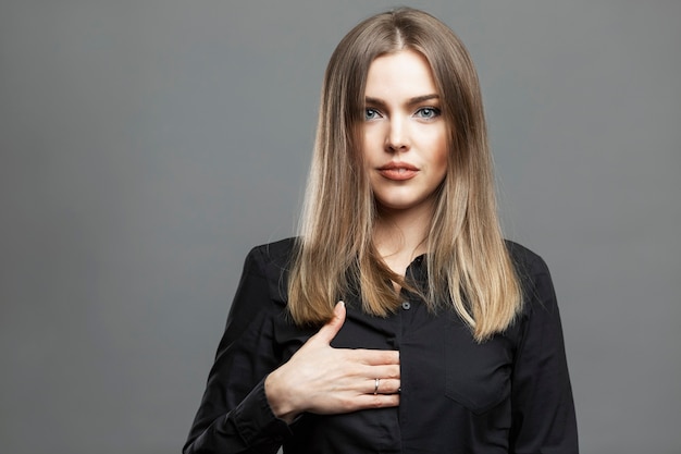 Young woman shows a hidden hand sign. Beautiful blonde in a black shirt. Masonic symbolism and the theory of the world conspiracy. Gray background.