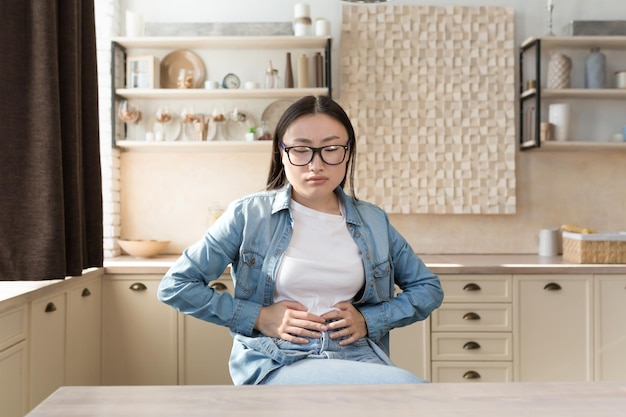 Young woman sick alone at home having severe stomach pain asian woman holding her stomach with hands