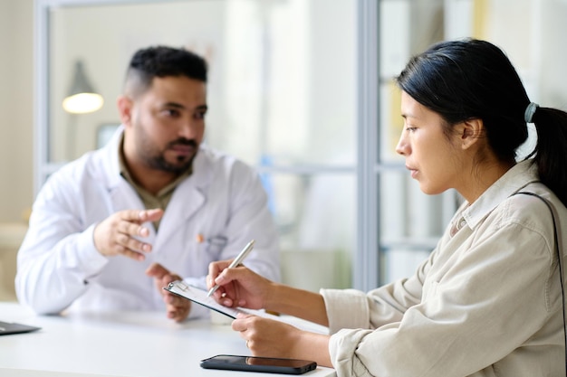 Young woman signing agreement for operation while having consultation with doctor in hospital