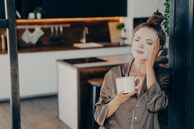 Young woman in silk pajamas staying at home and enjoying morning cup of coffee