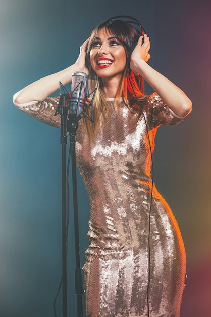 Photo a young woman singer with headphones in front of the microphone. sing with mouth wide open and with an expression of happiness on her face.