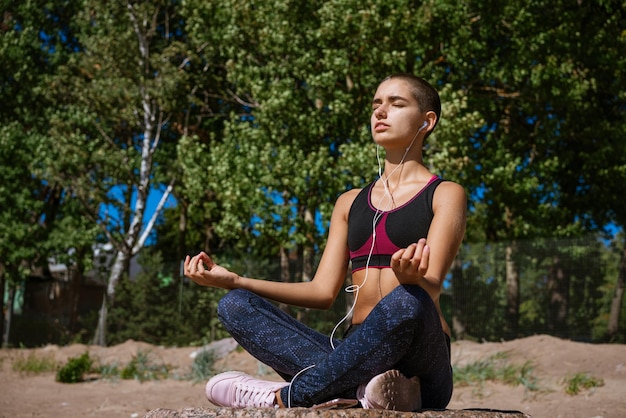 Photo young woman sits on beach on shore bay and meditates and listens to music