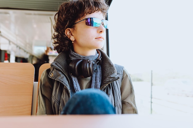 A young woman sits on a bus wearing sunglasses and a scarf