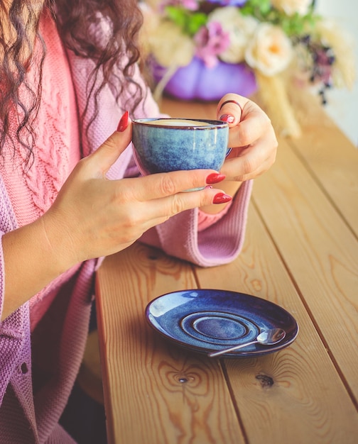 a young woman sits in a cafe and holds a cup of coffee in her hands.