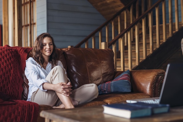 Young woman sits at home on the couch and looks at her laptop screen