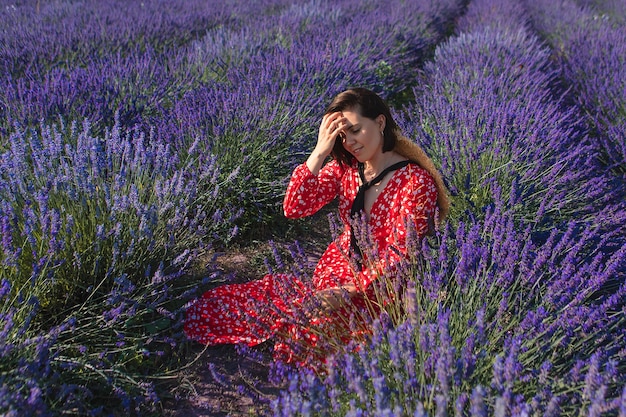 A young woman sits in a lavender field with a straw hat hanging around her neck