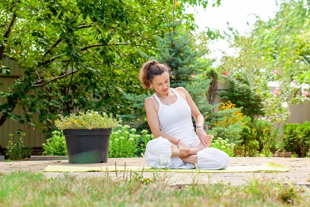 Young woman sits in lotus position helping with her hands practices yoga in the garden