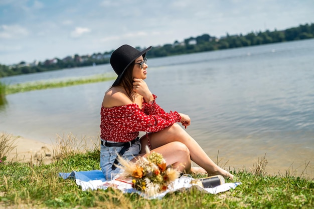 Young woman sits near pond and rest enjoys hot summer day at nature