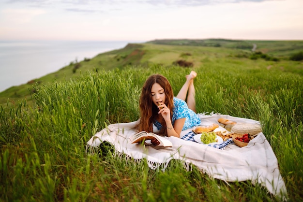 Young woman sits on a plaid with a book Summer picnic in nature Healthy food