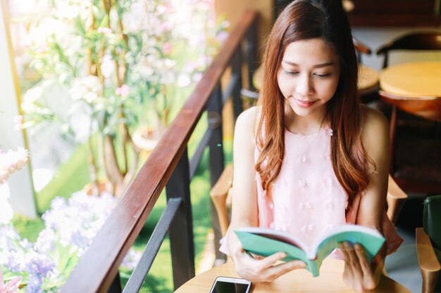 Young woman sits at a window in a cafe and read a book happily with a relaxing holiday.