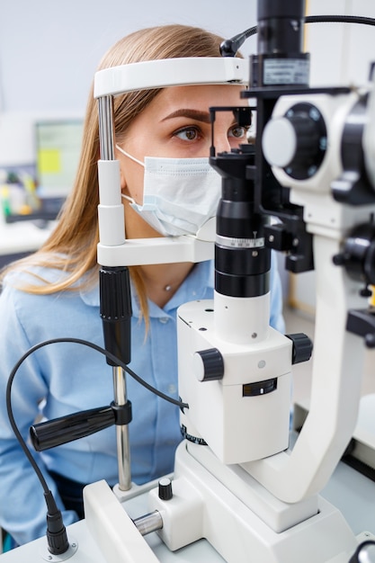 Young woman sitting in armchair looking at slit lamp during medical examination in eyes