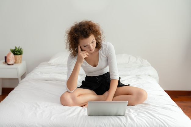 Young woman sitting on the bed in the bedroom with her laptop has a problem