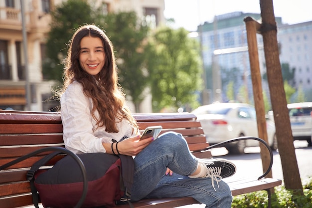 Young woman sitting on a bench in the city while using her mobile phone