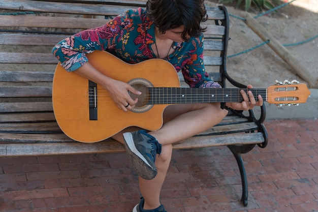 Young woman sitting on a bench playing the guitar in the park.