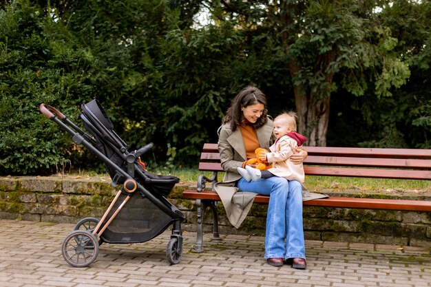 Young woman sitting on a bench with cute baby girl in the autumn park