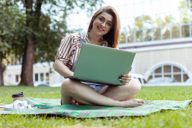 Young woman sitting on a blanket in the park and using computer