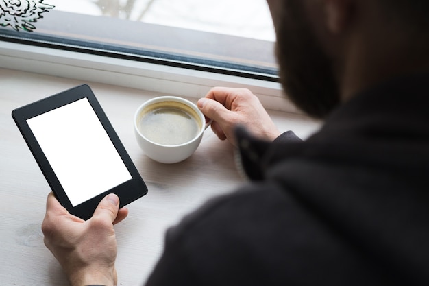 Young woman sitting by the window with an e-book