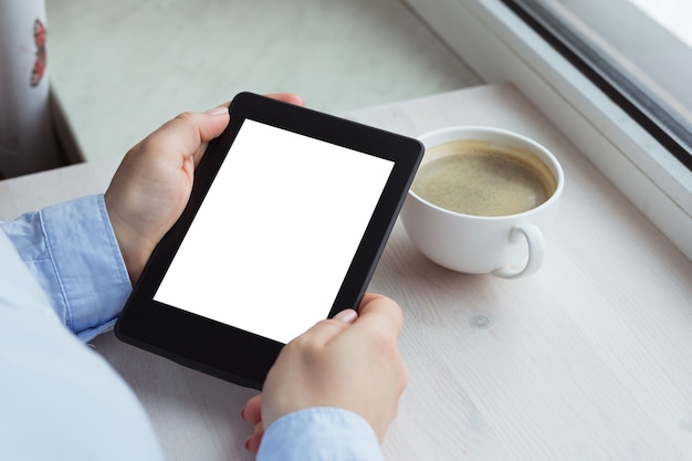 Young woman sitting by the window with an e-book