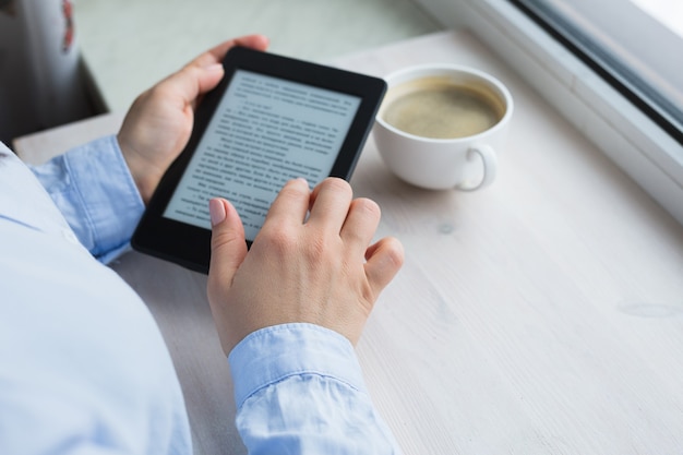 Young woman sitting by the window with an e-book