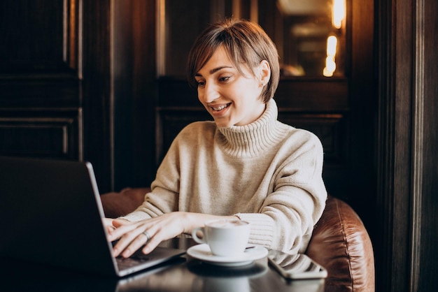 Young woman sitting in cafe drinking coffee and working on a computer