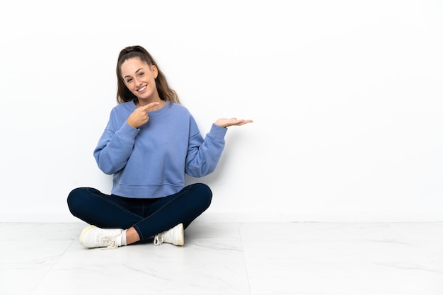 Young woman sitting on the floor holding copyspace imaginary on the palm to insert an ad