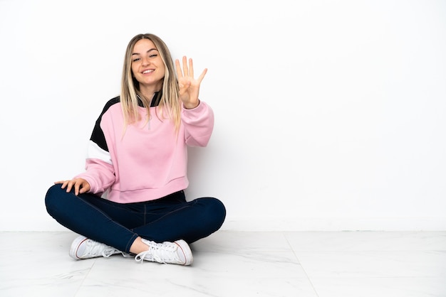 Young woman sitting on the floor at indoors happy and counting four with fingers