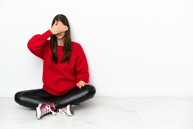 Young woman sitting on the floor isolated on white background covering eyes by hands. Do not want to see something