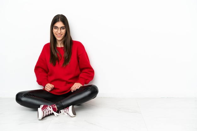 Young woman sitting on the floor isolated on white background laughing