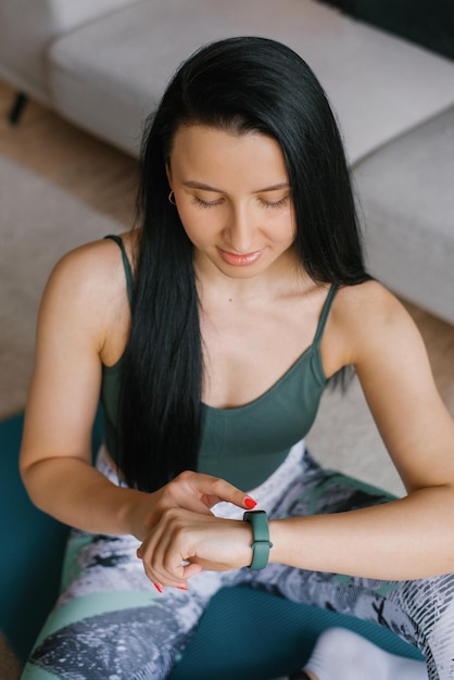 A young woman sitting on the floor and looking at her smartwatch in a cozy house