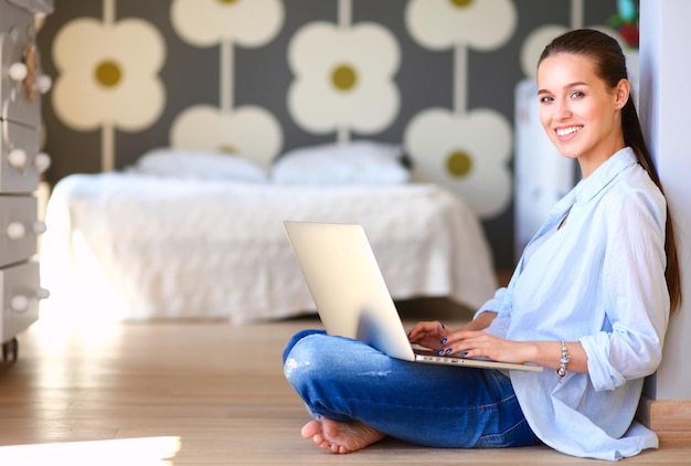 Young woman sitting on the floor near children's cot with laptop Young mom