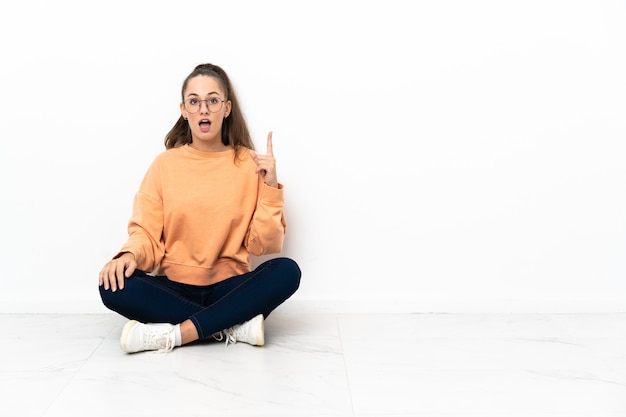 Photo young woman sitting on the floor thinking an idea pointing the finger up