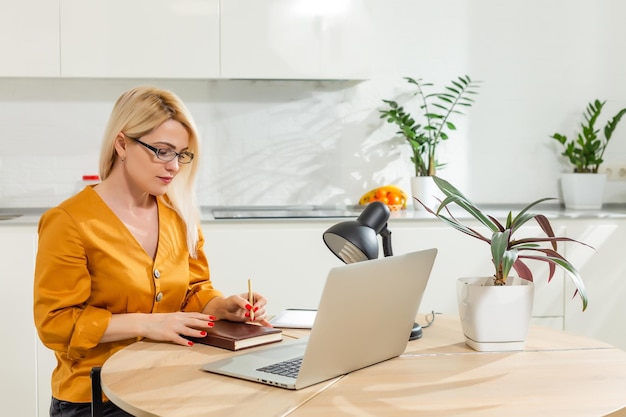 Young woman sitting in kitchen and working on laptop.