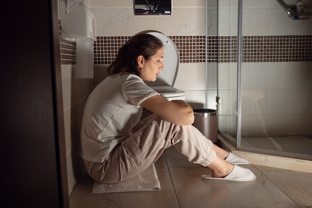 Young woman sitting near toilet