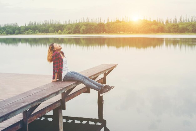 Photo young woman sitting on pier over lake during sunset