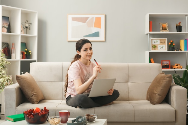 Young woman sitting on sofa behind coffee table holding and used laptop in living room