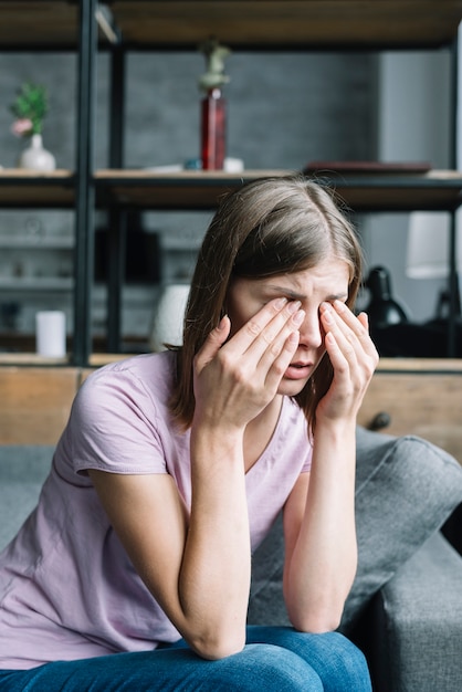 Young woman sitting on sofa having eye pain