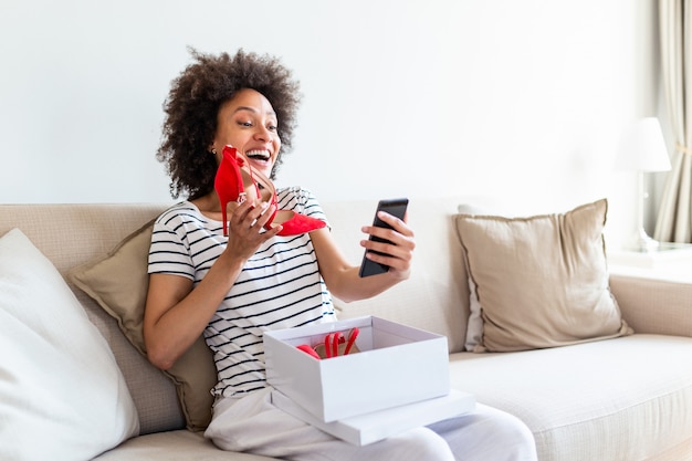 Young woman sitting on the sofa at home and face timing to show her new shoes